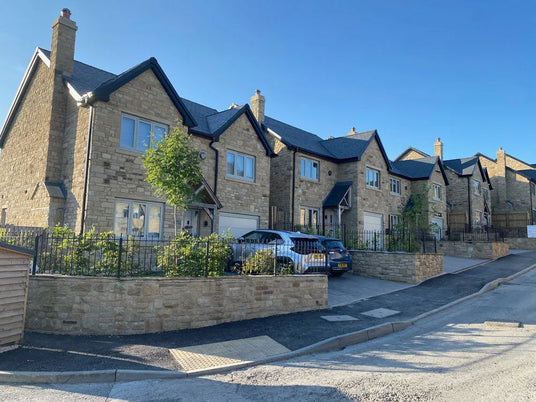 Row of stone houses with cars parked along a street on a clear day.