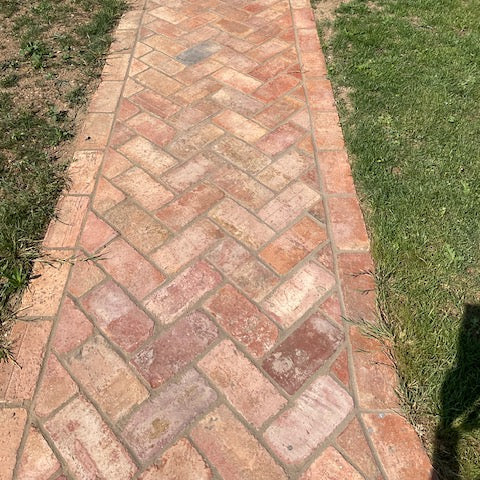 A brick pathway laid in a herringbone pattern, bordered by green grass on both sides.