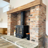 Wood-fired stove in a brick fireplace with a wooden mantel.
