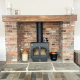 A brick slip fireplace with an oak beam mantel and a Yorkshire stone hearth, featuring a black wood stove.