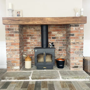A brick slip fireplace with an oak beam mantel and a Yorkshire stone hearth, featuring a black wood stove.