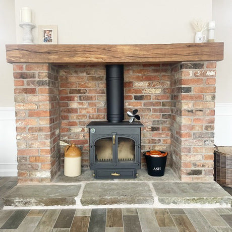 A brick slip fireplace with an oak beam mantel and a Yorkshire stone hearth, featuring a black wood stove.