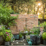 Garden scene with a brick wall, potted plants, and a sunlit sky.