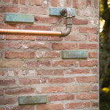 Brick wall with metal pipes and greenery in the background