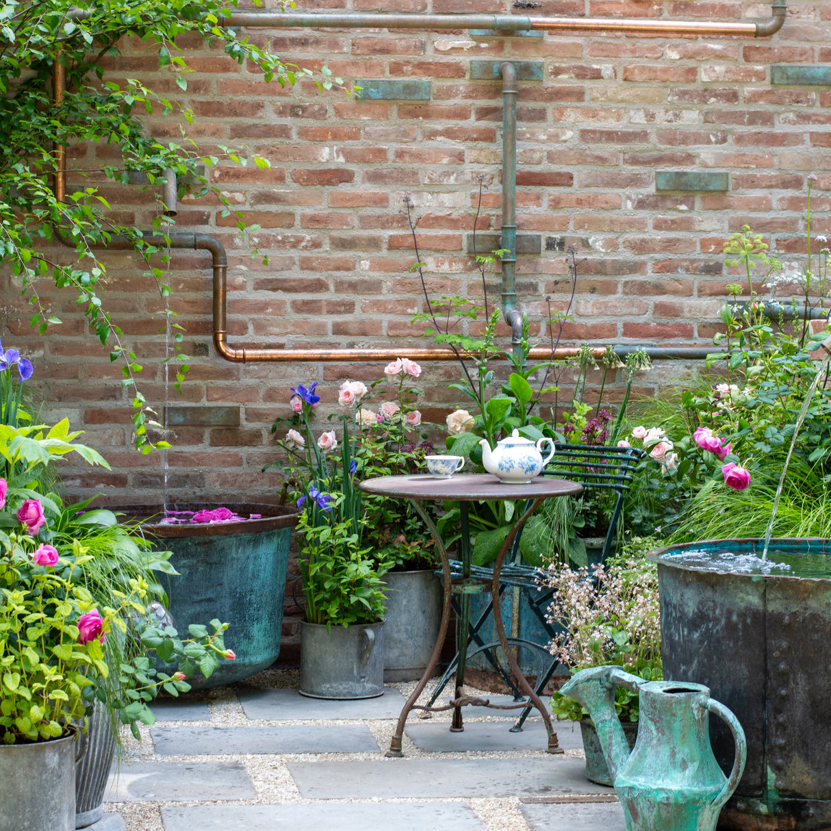 Outdoor garden scene with a brick wall, potted plants, and a small table.